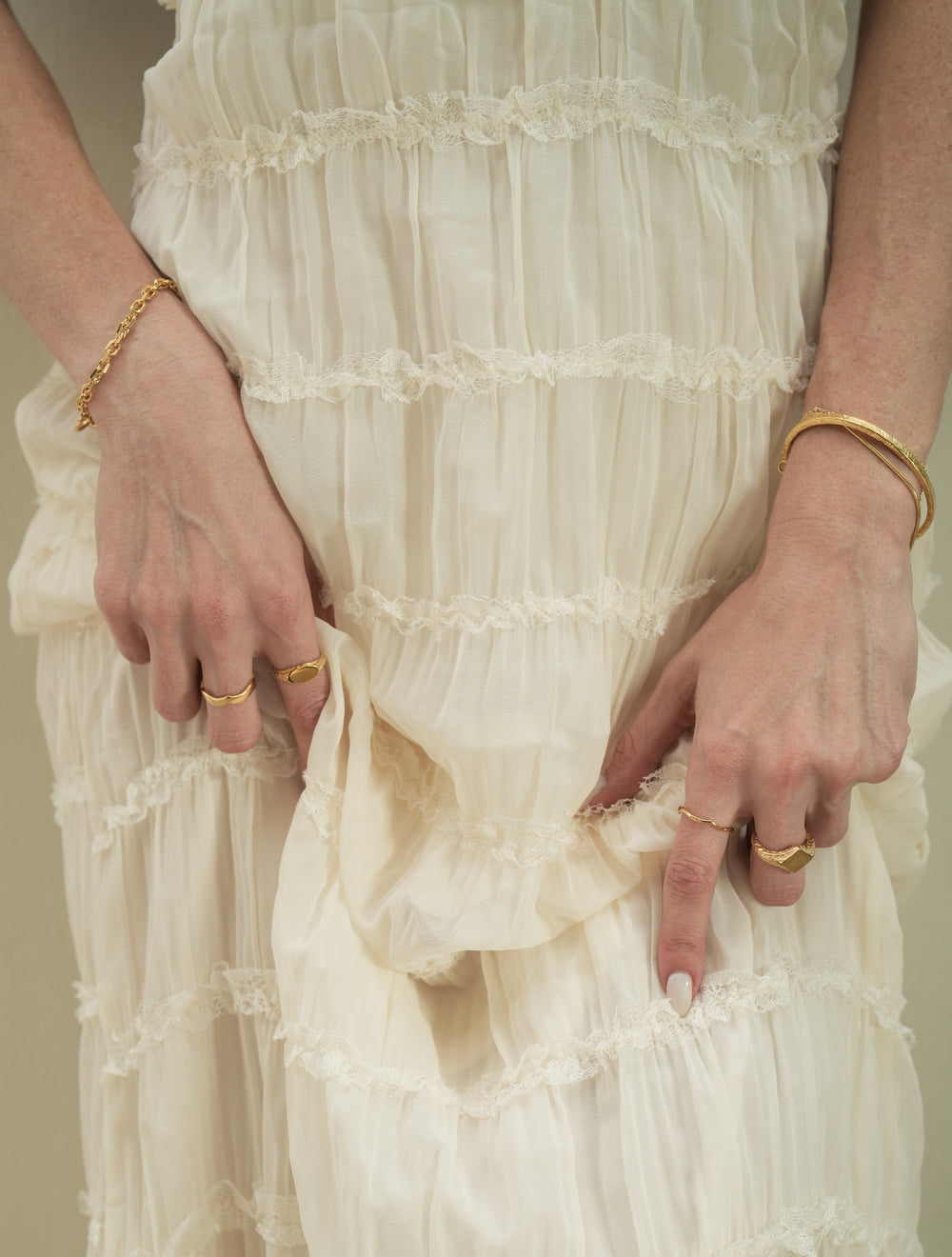 Founder of Nusands Emily Micari waist view photo both hands grabbing her white dress, right hand wearing 18k gold shacked bracelet, one wave ring on middle finger and mirrored signet ring on index on index finger. Left hand with stacked striking cuff and signature chain bracelet with suns out ring on middle finger and the other wave ring on index finger.