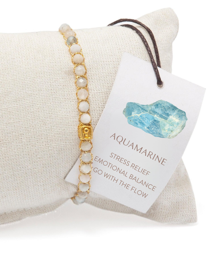 Aquamarine gemstone bracelet on a cushion, accompanied by a card with text and an image of the stone properties.