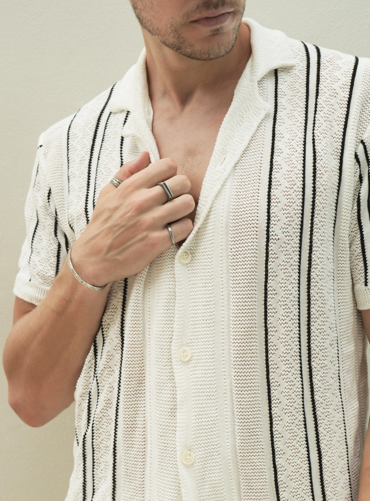 Founder of Nusands Corey micari front view of chest, right hand infront of chest, look to the left. Striking Cuff sterling silver on right wrist, blade ring on thumb, line in the sand on middle finger, stacker ring on pinky.