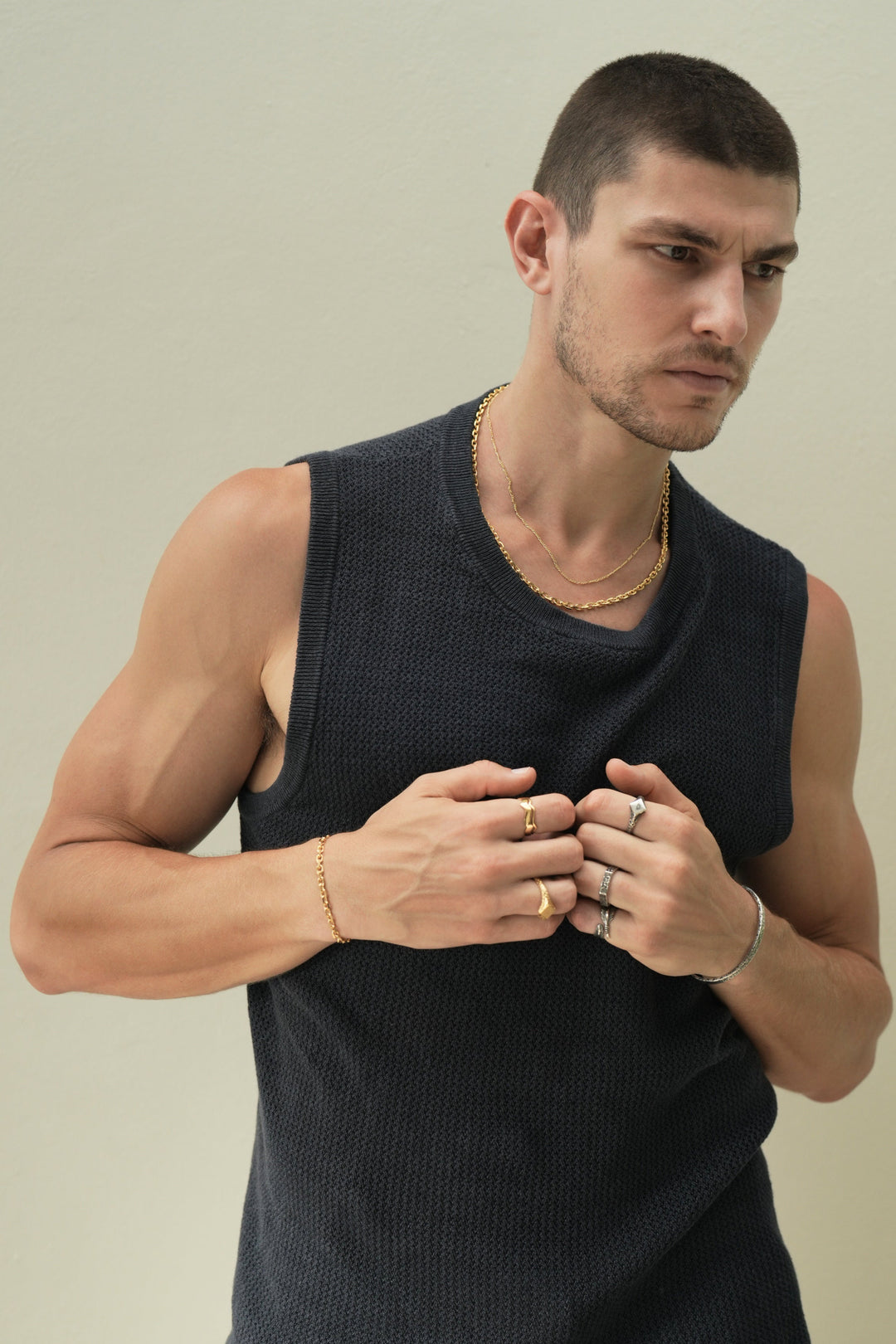 Founder of Nusands Corey Micari waist up front on view with him looking to the left of the camera wearing a blue singlet, arms bent, right bicep flexed with hands touching slightly in fists. Stacked signature chain and shackled 18k gold necklaces around his neck. Stacked wave rings on right hands index finger, suns out ring on another. Matching shackled bracelet around his wrist. Sterling silver blade ring on left hands pinky, six base on ring finger and suns out on index, Striking cuff around his wrist.