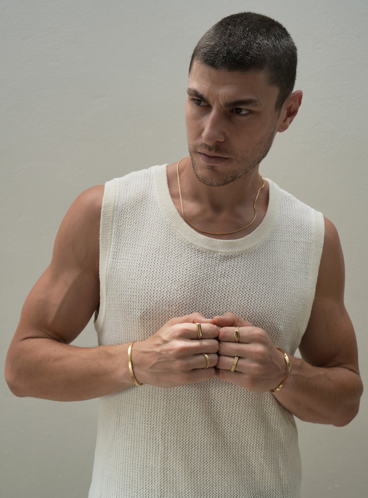 Founder of Nusands Corey Micari wearing 18k gold roped in necklace around neck, right hand with stirking cuff, line in the sand and stacker ring. Modest cuff on left wrist, mirrored signet and six base ring on hand fists together front profile, look away to right of camera, waist high view, white singlet on.