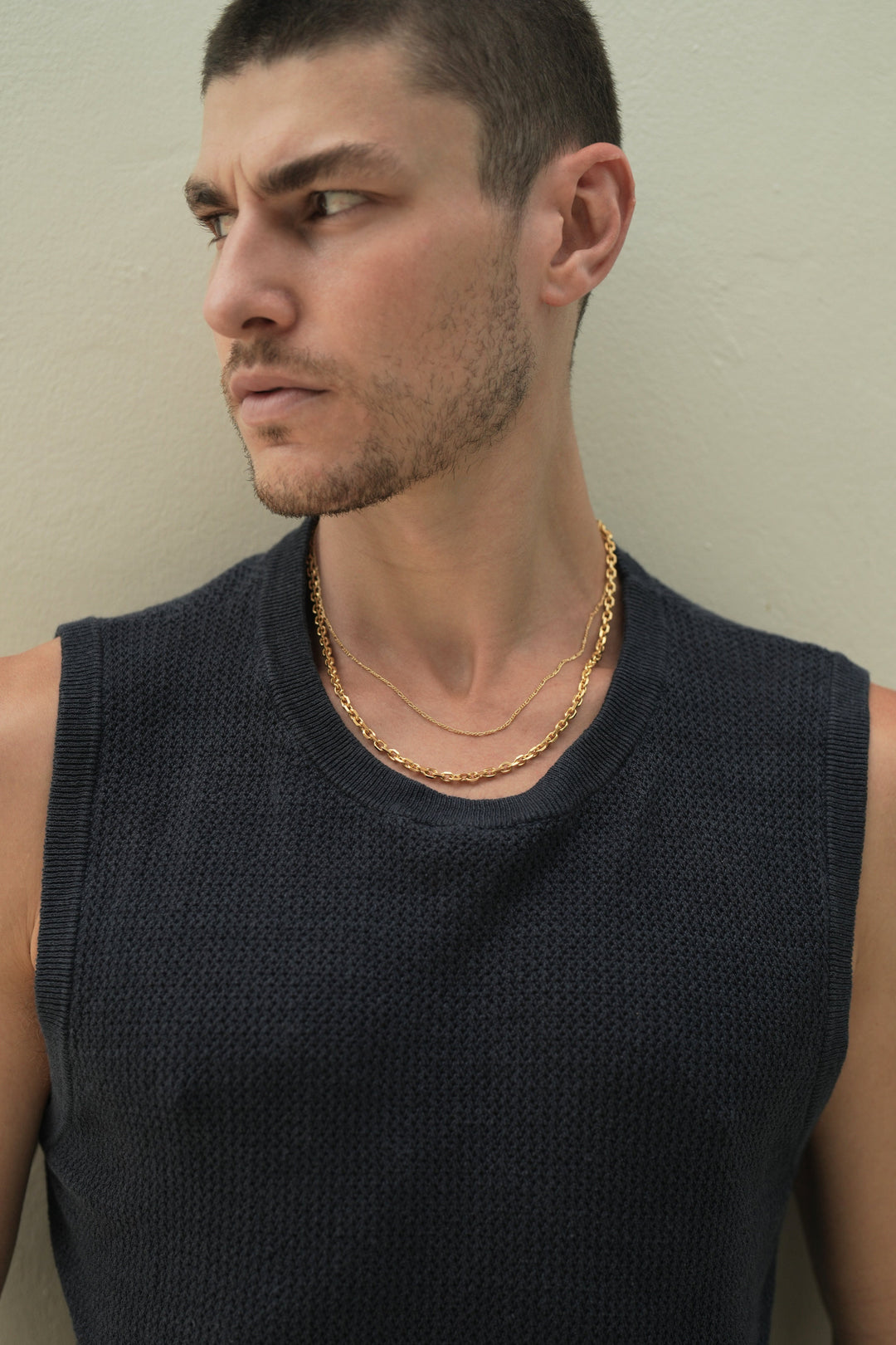 Founder of Nusands Corey Micari chest up front on view with him looking to the right of the camera wearing a blue singlet. Stacked signature chain and shackled 18k gold necklaces around his neck.