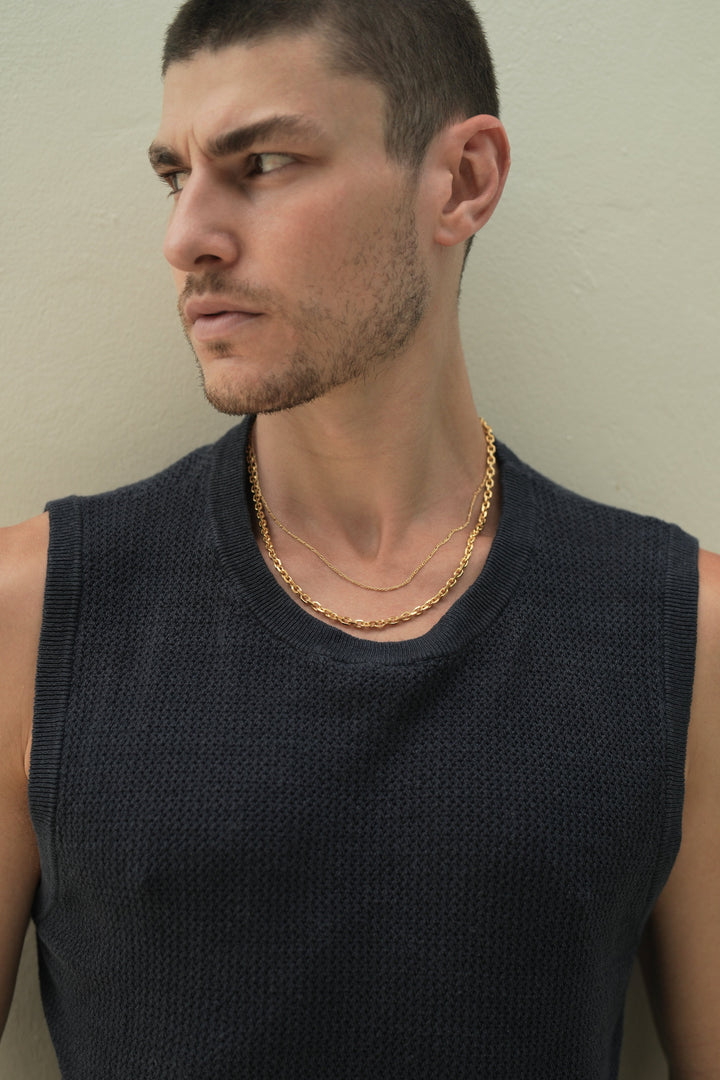 Founder of Nusands Corey Micari chest up front on view with him looking to the right of the camera wearing a blue singlet. Stacked signature chain and shackled 18k gold necklaces around his neck.