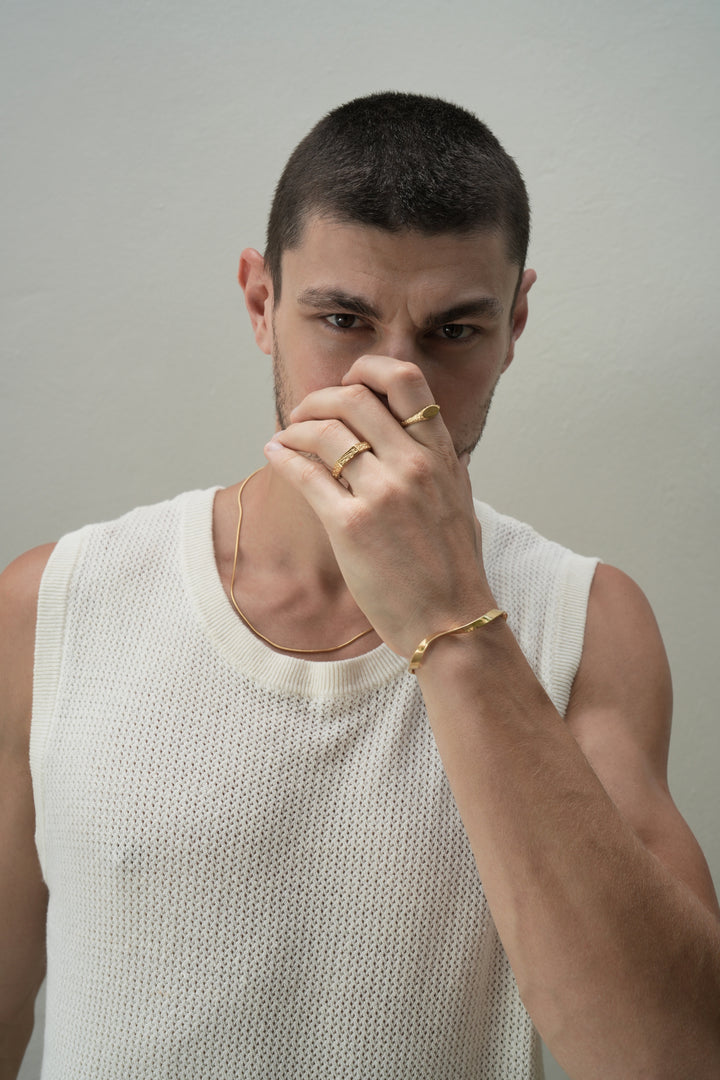 Founder of Nusands Corey Micari front profile right hand on face looking at camera 18k gold roped in necklace around neck, left hand covering bottom half of face, mirrored signet on index finger, six base ring on ring finger. Modest cuff around wrist.