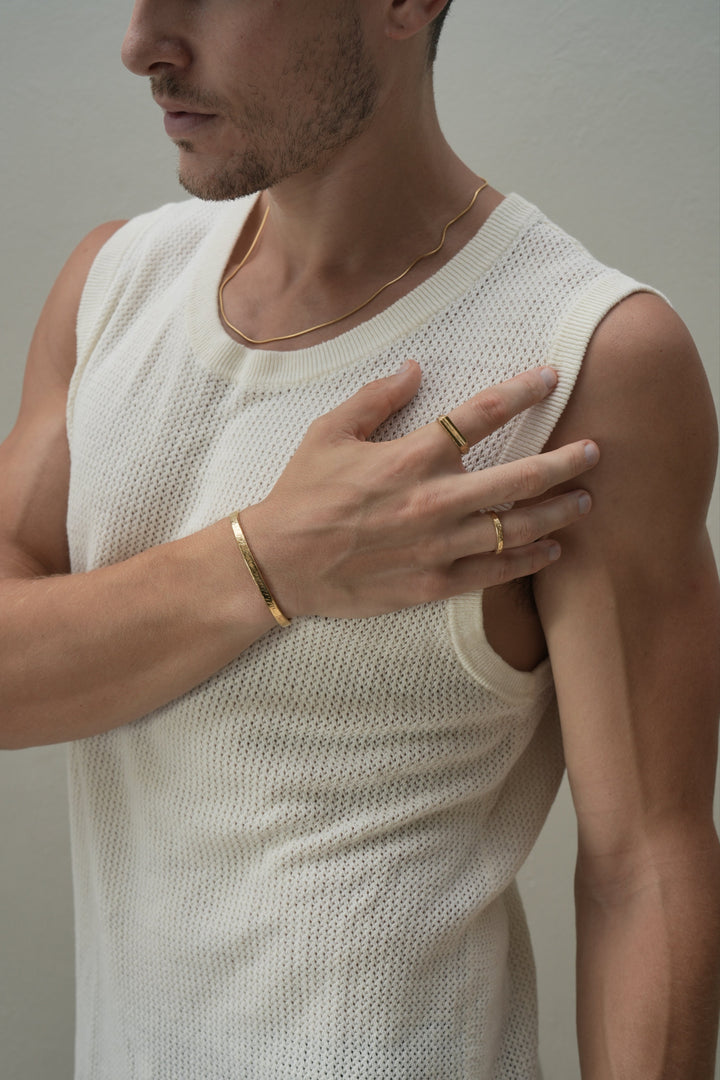 Founder of Nusands Corey Micari front profile wearing a range of 18k gold, roped in necklace, striking cuff and stacker and line in the sand rings on right hand as it comes across his left peck.