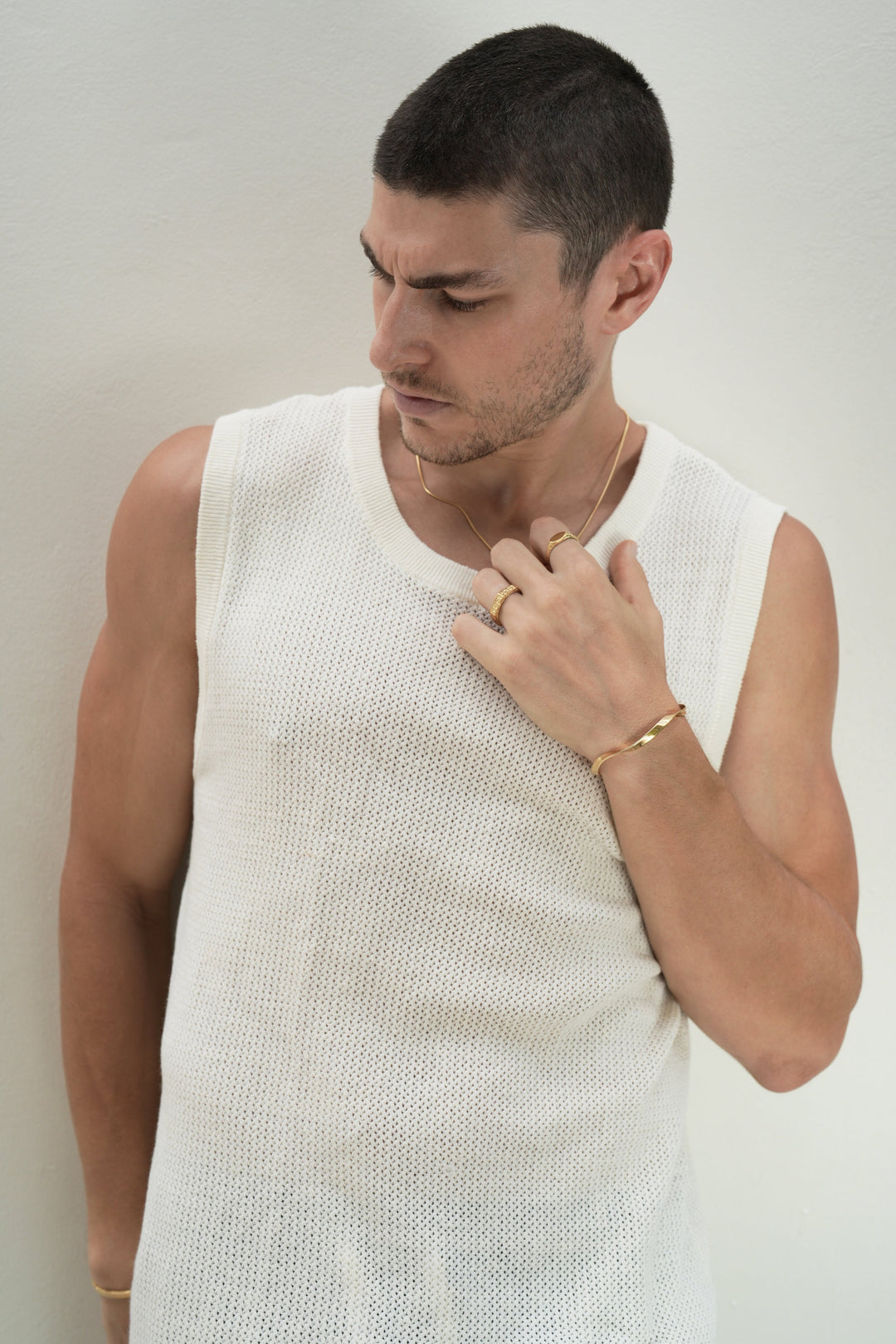 Founder of Nusands Corey Micari chest and head shot, look away to the right. Left hand to 18K Gold Roped in necklace, mirrored signet and six base rings on fingers, modest cuff on wrist.