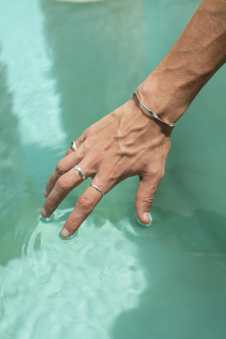 Founder of Nusands Corey Micari, right hand on top of water, Sterling Silver modest cuff on wrist, mirrored signet ring on pinky and wave rings unstacked thicker on middle finger and thinner on index finger.