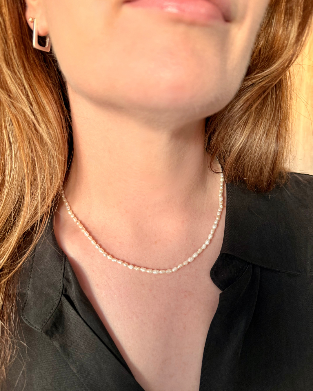 Pearl necklace worn by a woman wearing a black top and wearing Nusands' silver rectangle earrings.