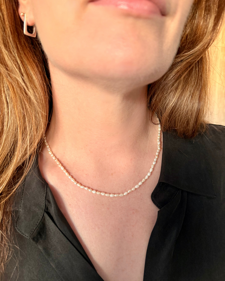 Pearl necklace worn by a woman wearing a black top and wearing Nusands' silver rectangle earrings.