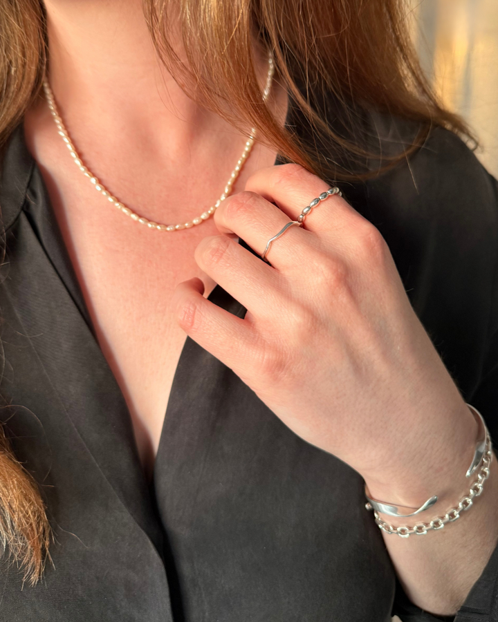 Close-up of a woman wearing a pearl necklace, silver ring, and bracelets.