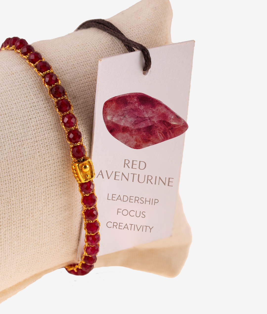 Red beaded bracelet with gold accents on a beige pillow next to a card describing red aventurine properties.