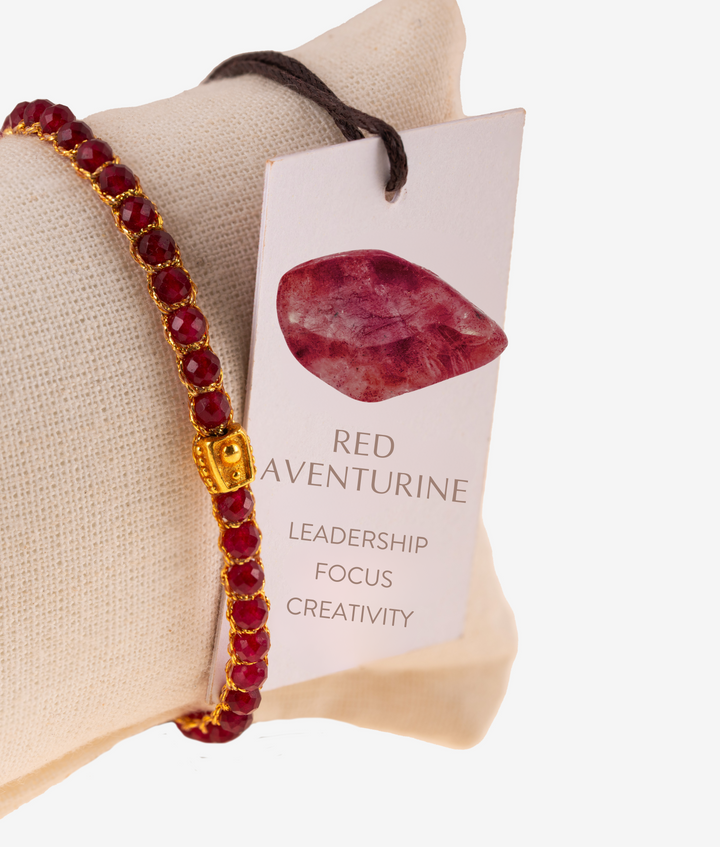 Red beaded bracelet with gold accents on a beige pillow next to a card describing red aventurine properties.
