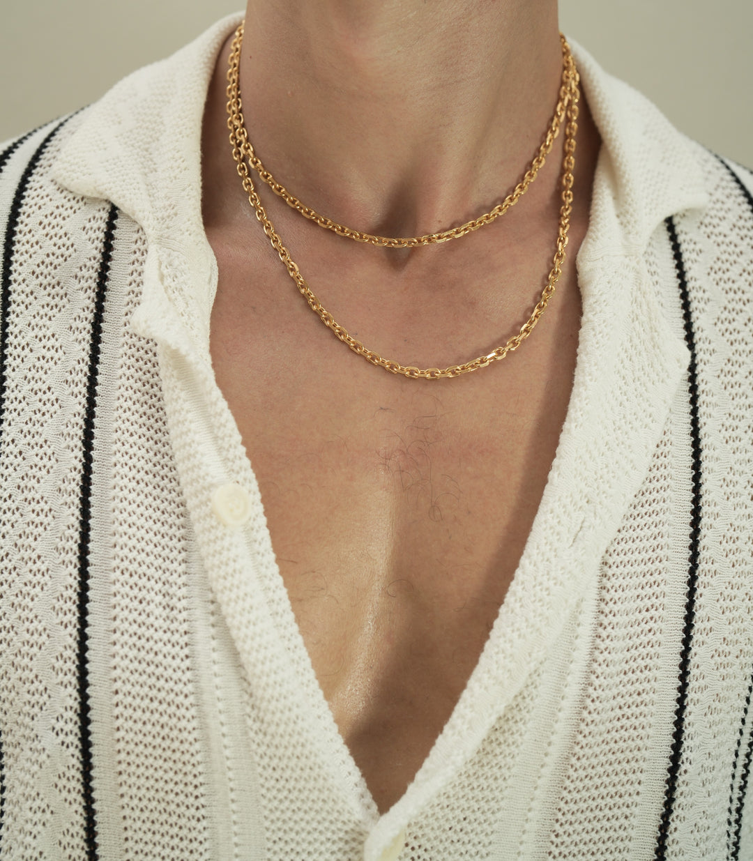 Founder of Nusands Corey Micari chest shot of open white shirt with black stripes unbuttoned to reveal stacked 45 and 55cm 18k gold shackled necklaces