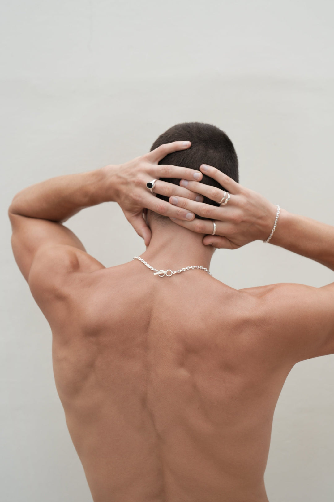 Founder of Nusands Corey Micari waist up shot of his back with hands grasped behind his head. Wearing Shiny sterling silver midnight onxy ring on his left middle finger, stacked wave rings with stacker ring on his right hand, shackled bracelet matching with shackled necklace.