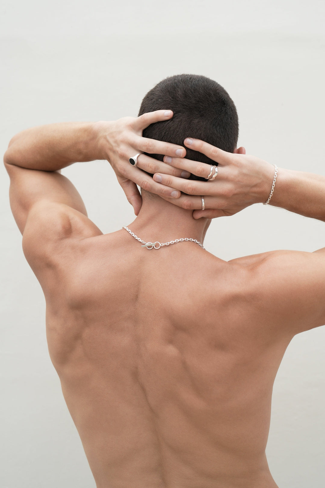 Founder of Nusands Corey Micari waist up shot of his back with hands grasped behind his head. Wearing Shiny sterling silver midnight onxy ring on his left middle finger, stacked wave rings with stacker ring on his right hand, shackled bracelet matching with shackled necklace.