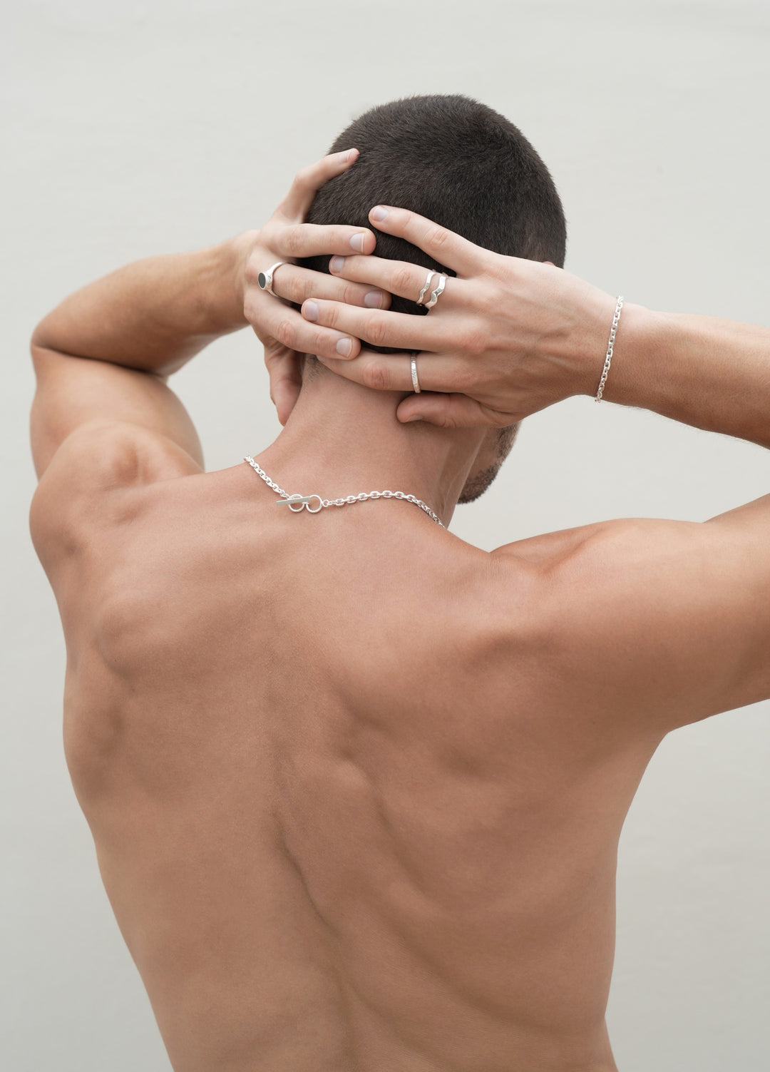 Founder of Nusands Corey Micari waist up shot of his back with hands grasped behind his head. Wearing Shiny sterling silver midnight onxy ring on his left middle finger, stacked wave rings with stacker ring on his right hand, shackled bracelet matching with shackled necklace.