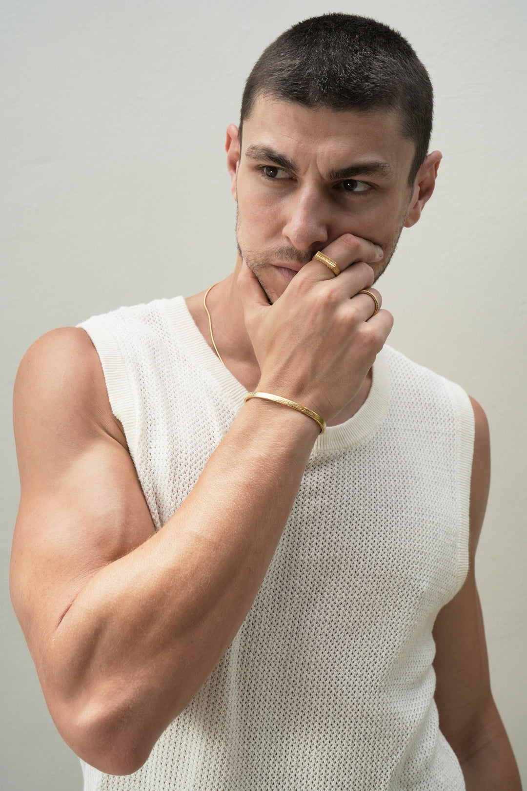 Founder of Nusands Corey Micari front profile right hand on face looking away from camera wearing 18k gold striking cuff, stacker and line in the sand rings on right hand. Roped in necklace around neck.