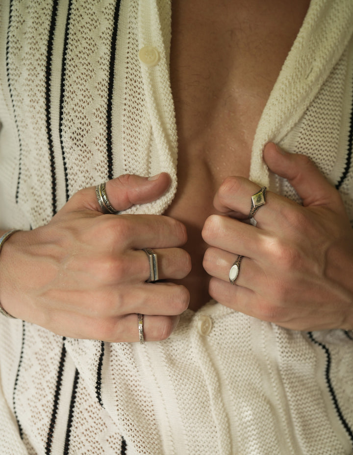 Founder of Nusands Corey Micari front view close up of chest, half unbuttoned white and black striped shirt both hands clasping the inside. Mirrored signet and suns out rings on left hand, striking cuff, blade, line in the sand and stacker rings on right hand.