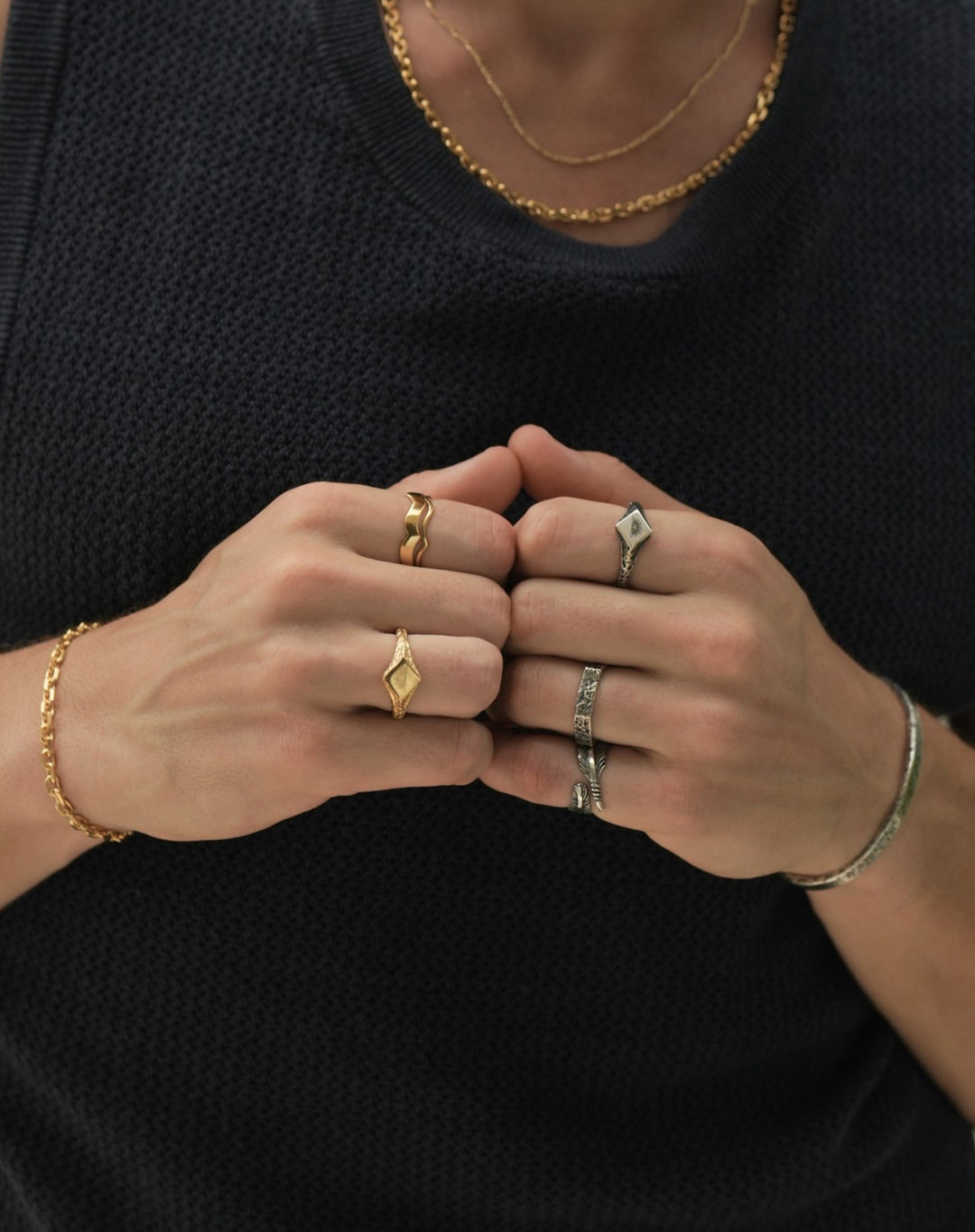 Founder of Nusands Corey Micari zoomed in chest shot wearing navy singlet, both hands meeting together in fists. Wearing 18K Gold stacked signature chain and shackled necklaces around neck, shackled bracelet on right wrist with suns out ring on a finger, stacked wave rings on another. His left arm is all sterling silver jewellery, stirking cuff on wrist, suns out, stacker and blade rings on hand.