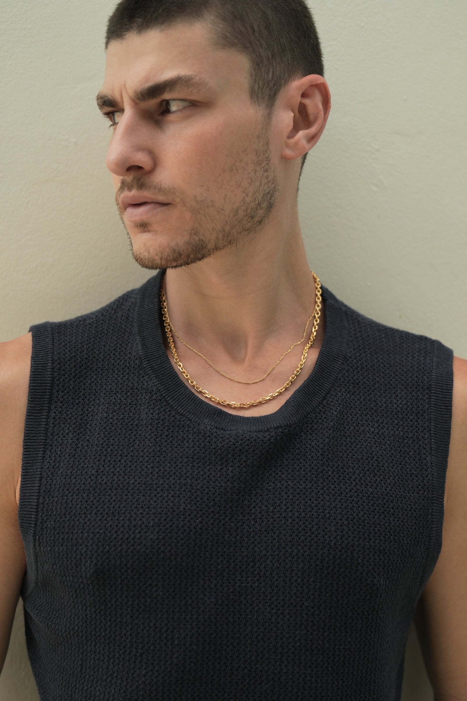 Founder of Nusands Corey Micari chest up front on view with him looking to the right of the camera wearing a blue singlet. Stacked signature chain and shackled 18k gold necklaces around his neck.
