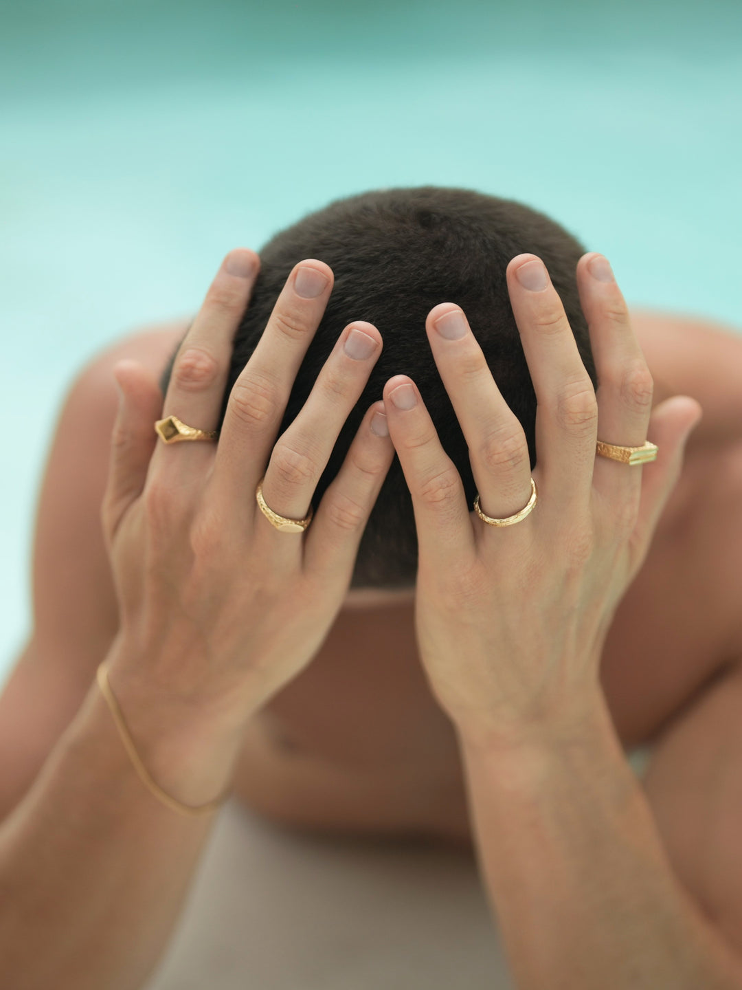 Founder of Nusands Corey Micari chest up shot in pool, hands covering head. Wearing 18k Gold roped in bracelet on right hand, suns out ring on index finger, mirrored signet on another. Left hand has stacker ring on ring finger, line in the sand on index.