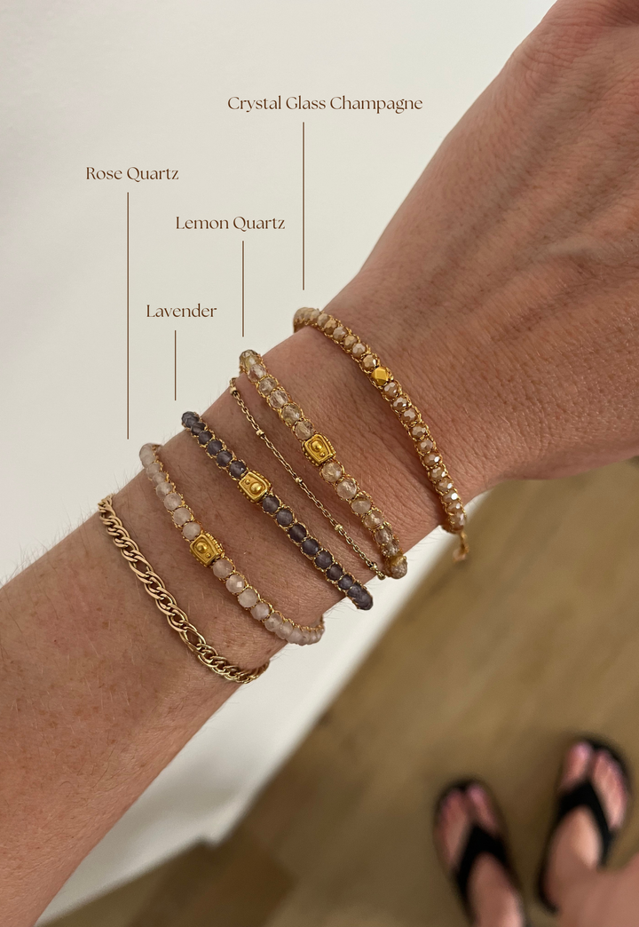 Collection of handmade crystal gemstone bracelets on a woman's wrist with name labels