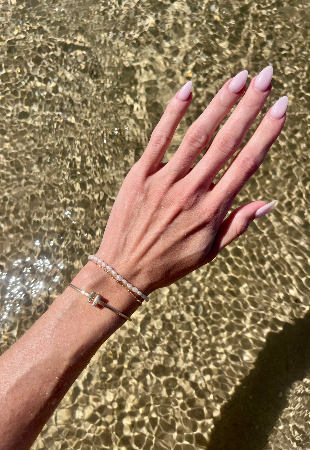 Emily wearing Unisex Pearl Bracelet on her left arm hovering it over the top of water to show the freshwater pearls.