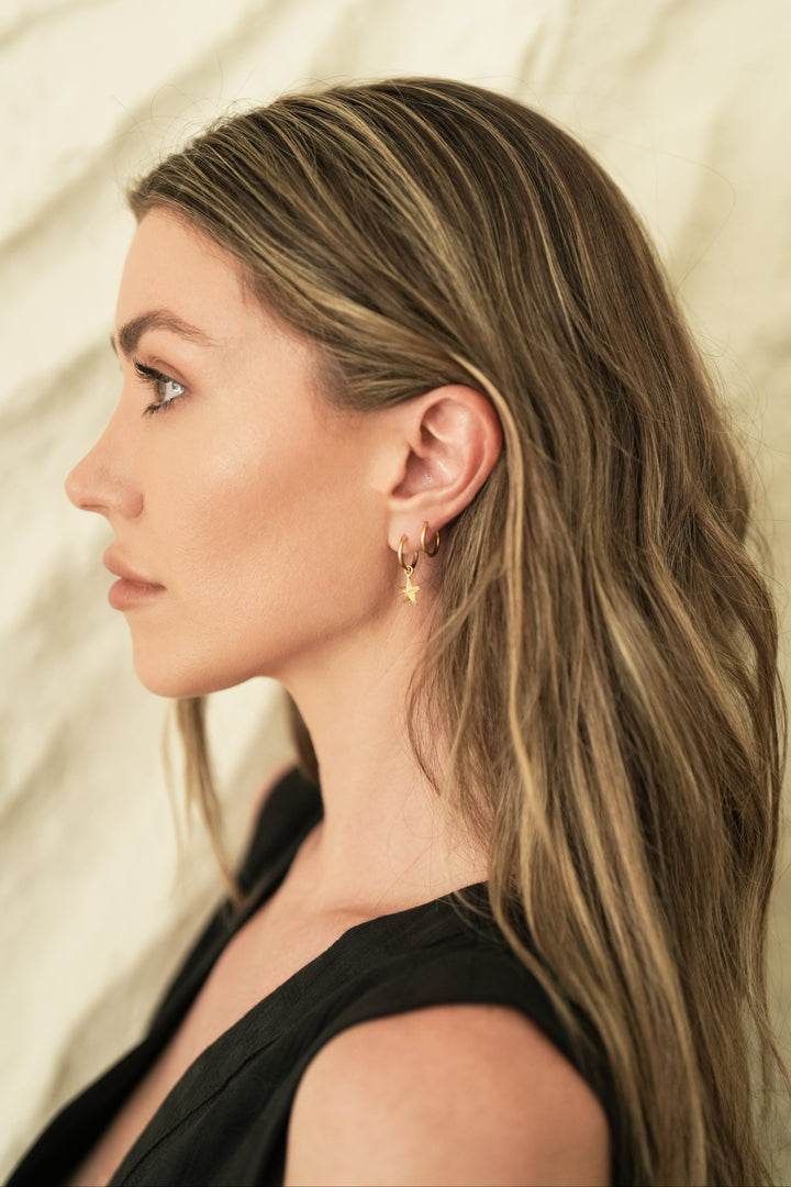 Founder of Nusands Emily Micari side profile wearing 18k gold round hoop earring with removable star charms.