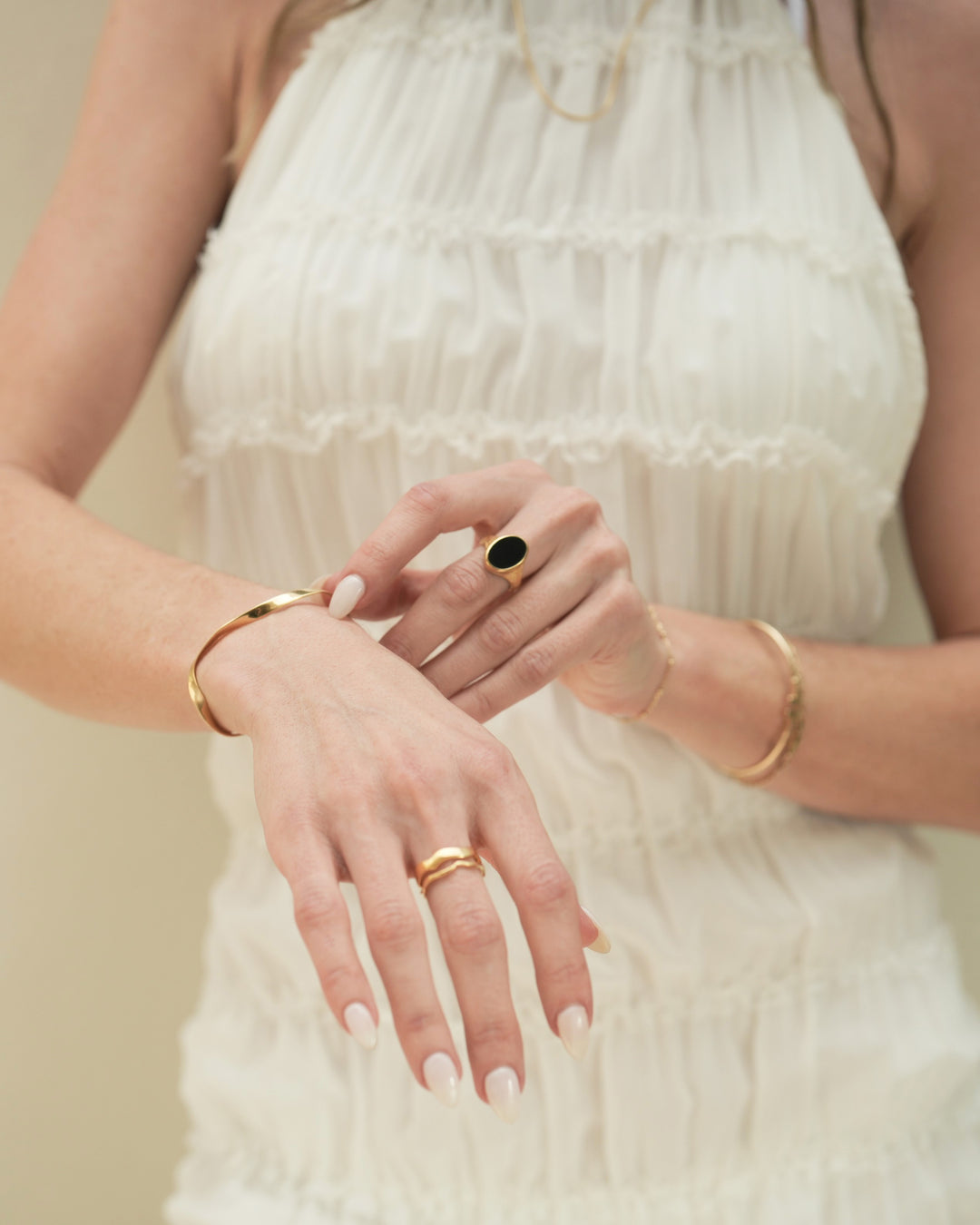 Founder of Nusands Emily Micari, chest view with left arm wearing 18k gold striking cuff layered with signature chain bracelet and midnight onyx ring on middle finger, slightly grasping the modest cuff around her right wrist the also wears a stacked pair of wave rings.