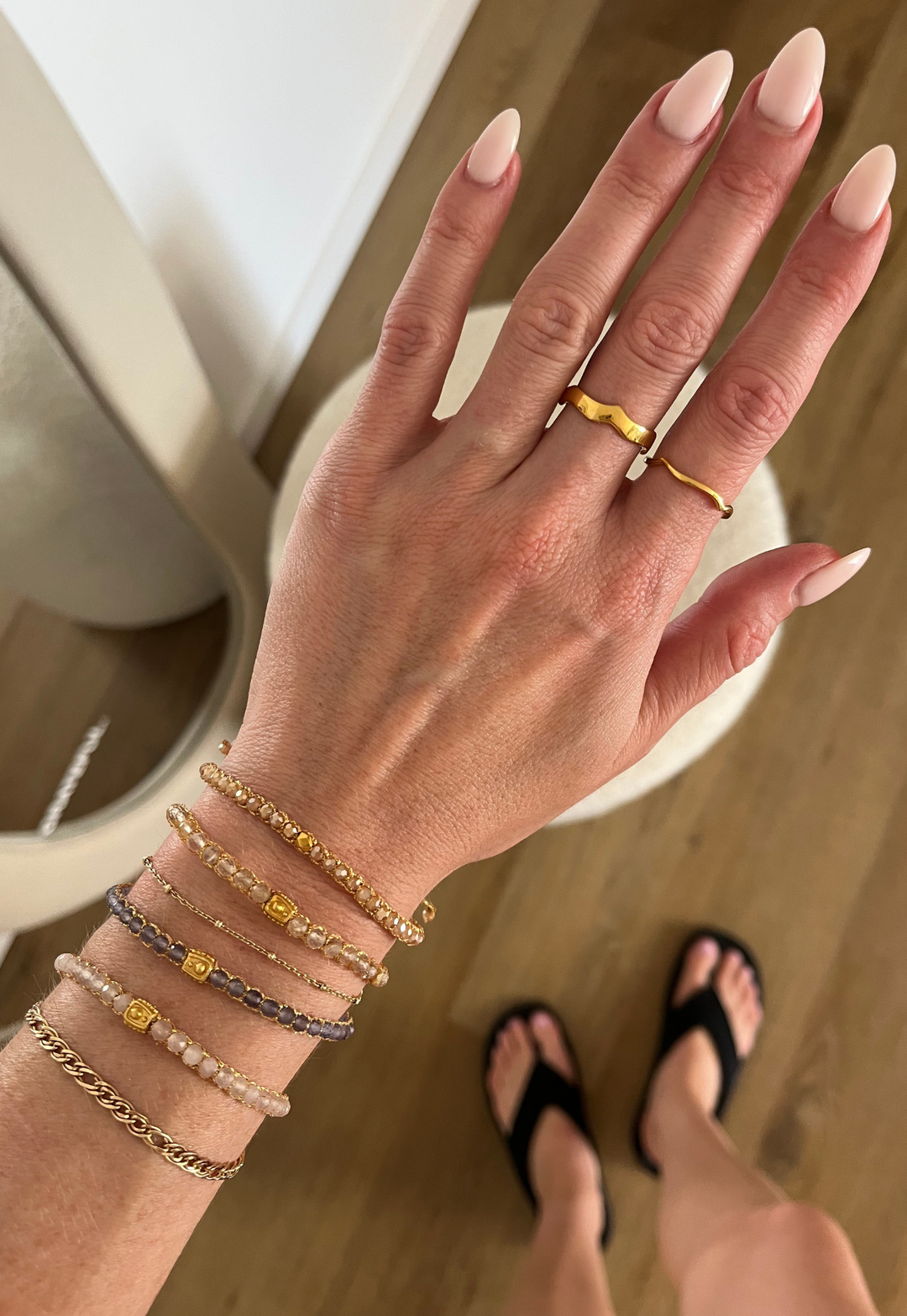Woman wearing multiple gemstone bracelets on her wrist with gold wave rings