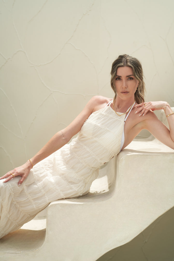 Founder of Nusands Emily Micari laying on her left side up a set of stairs facing the camera. Right arm is rested straight down the side of her body, 18k shackled bracelet on her wrist, mirrored signet and stacker rings on her fingers. Shackled bracelet around her neck, her left arm is bent, left hand resting gently next to her neck wearing stacked striking cuff with signature chain bracelet on her wrist, suns out ring on her finger.