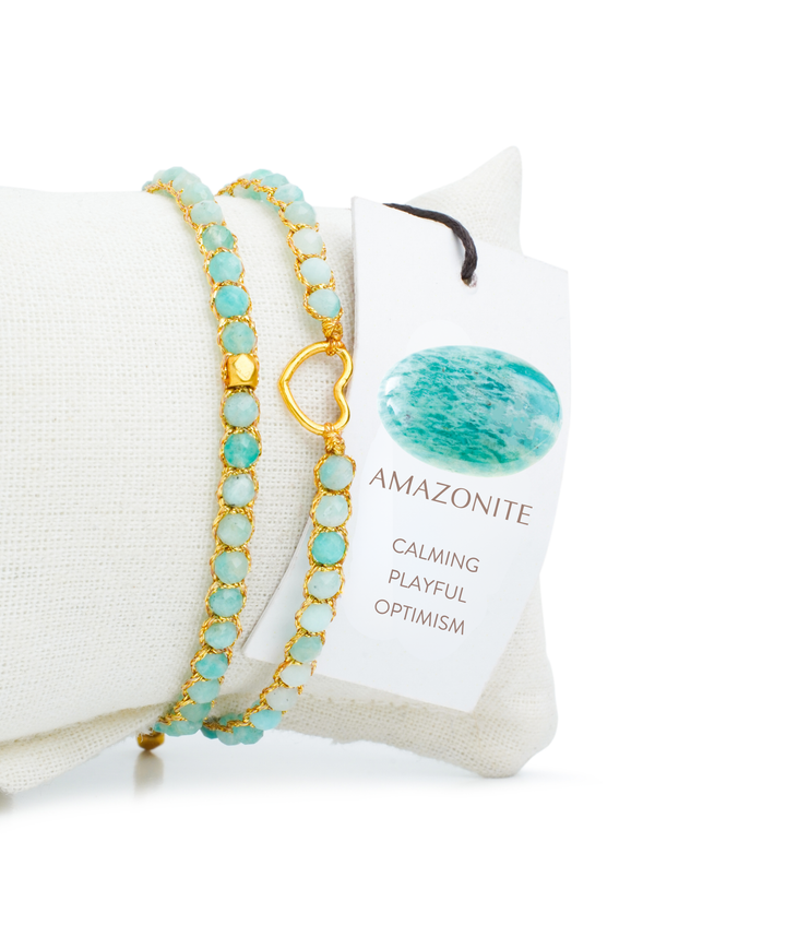 Turquoise beaded bracelet with gold accents on a white cushion, next to a card labeled 'Amazonite'.