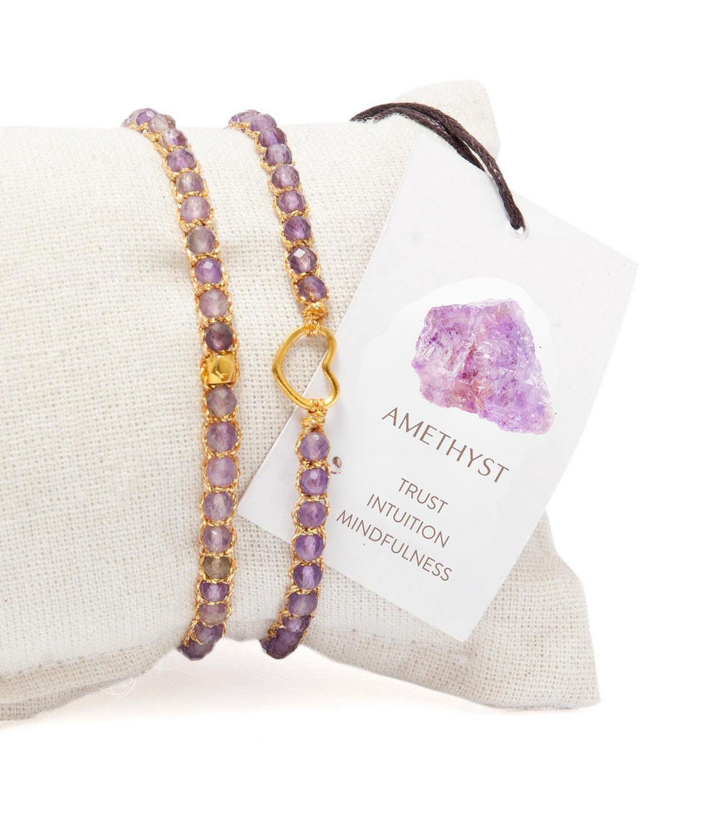 Purple beaded bracelet with gold accents on a white cushion, next to a card labeled 'Amethyst'.