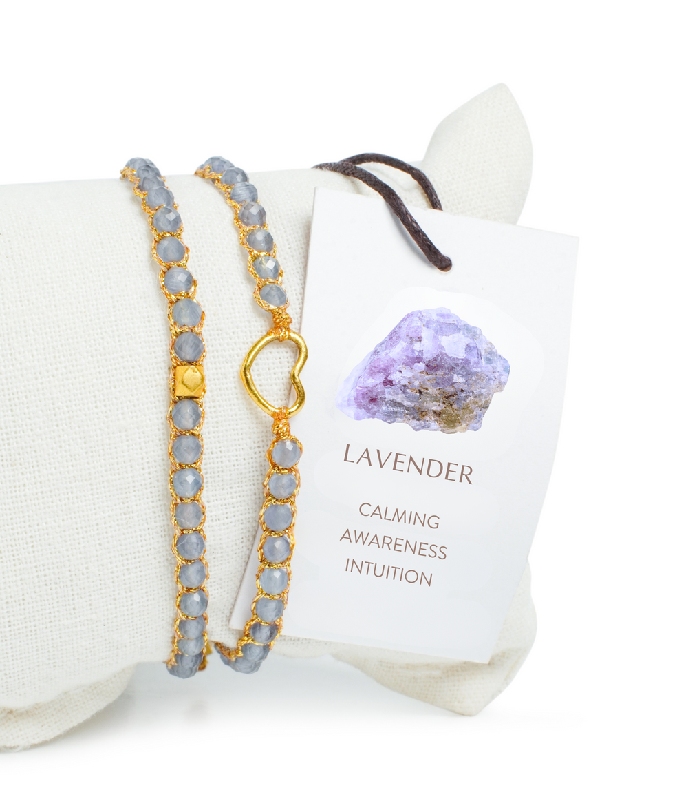 Lavender gemstone bracelet on a white pillow with an information card