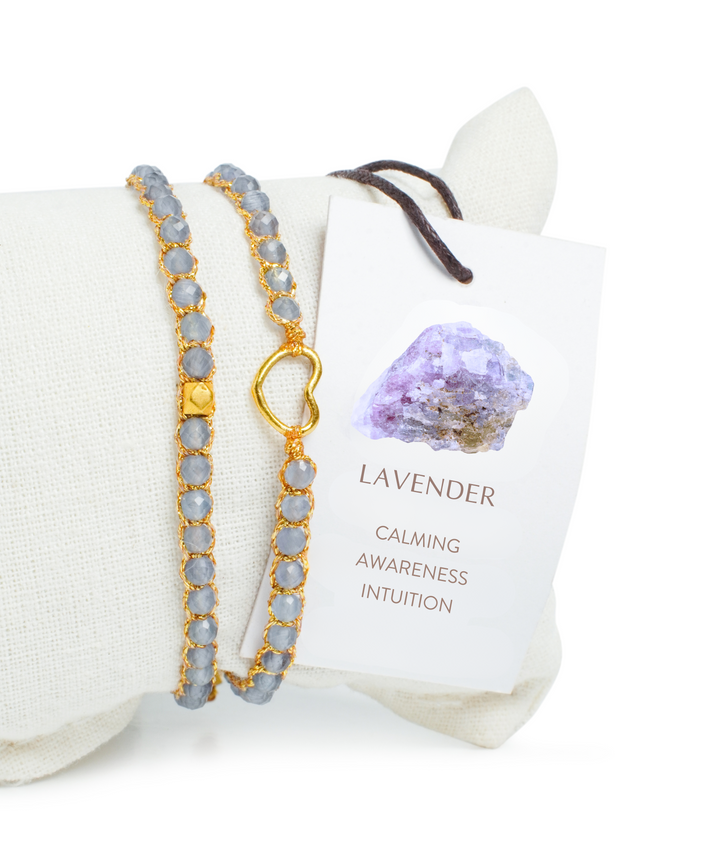 Lavender gemstone bracelet on a white pillow with an information card