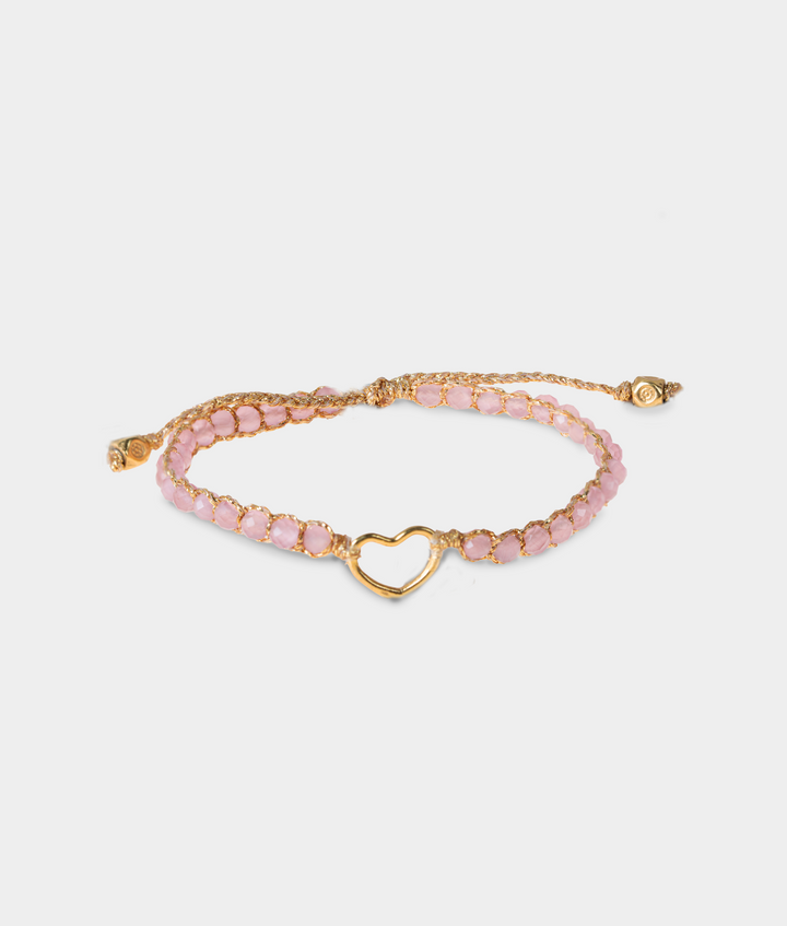 Gold bracelet with pink gemstones and a gold heart charm on a white background