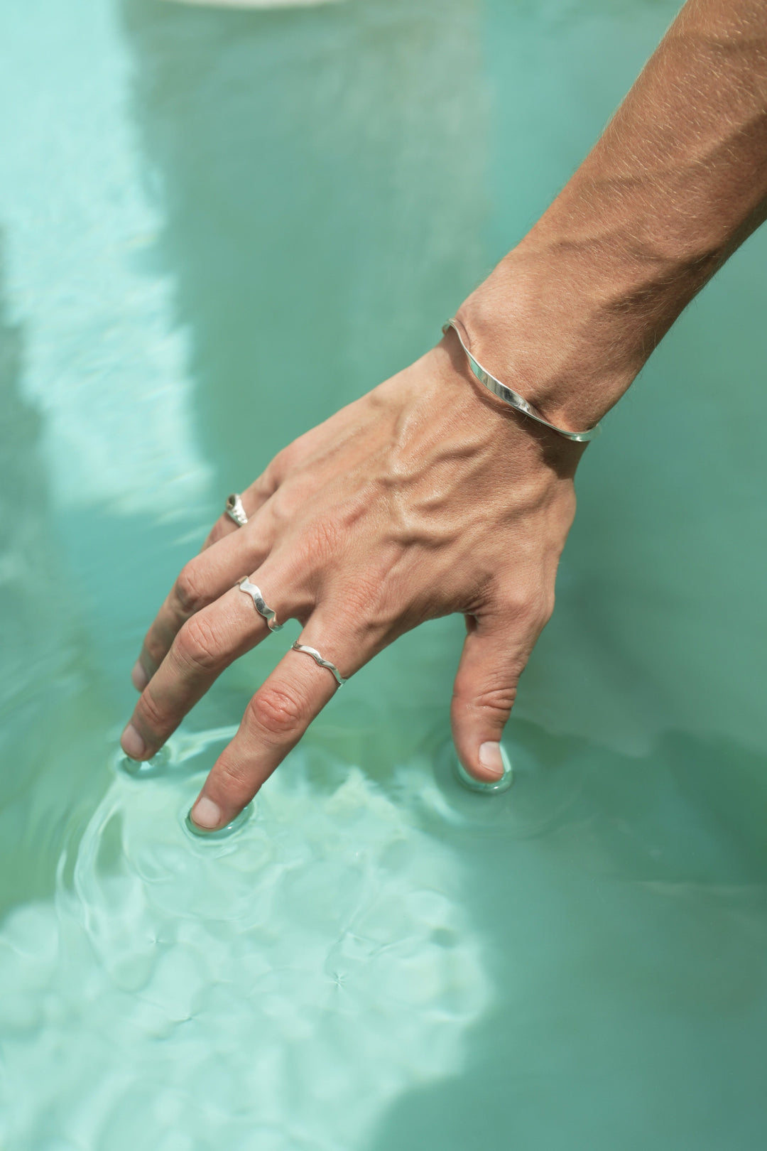 Founder of Nusands Corey Micar, right hand on top of water, Sterling Silver modest cuff on wrist, mirrored signet ring on pink and wave rings unstacked on separate fingers.