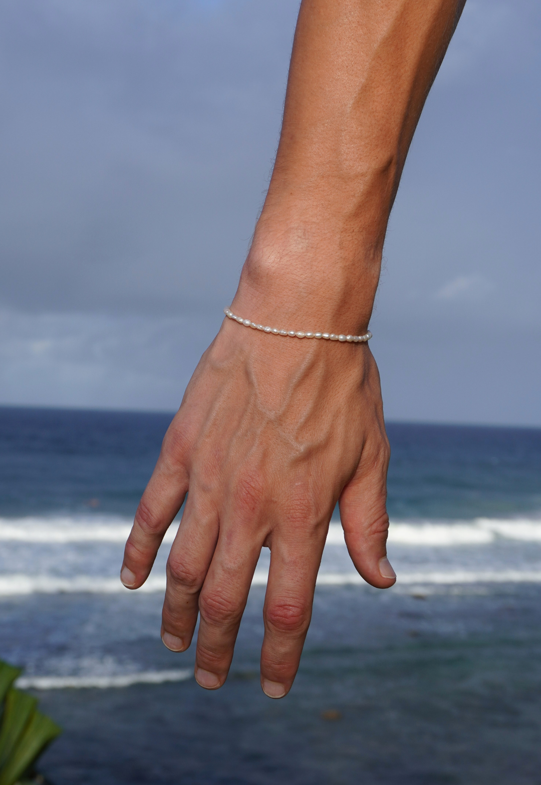 Male hand wearing the pearl bracelet with ocean in the background