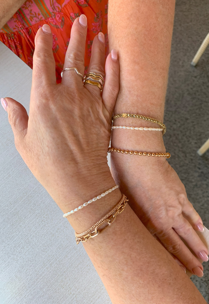 Two hands wearing the pearl bracelets with gold jewelry on a neutral background