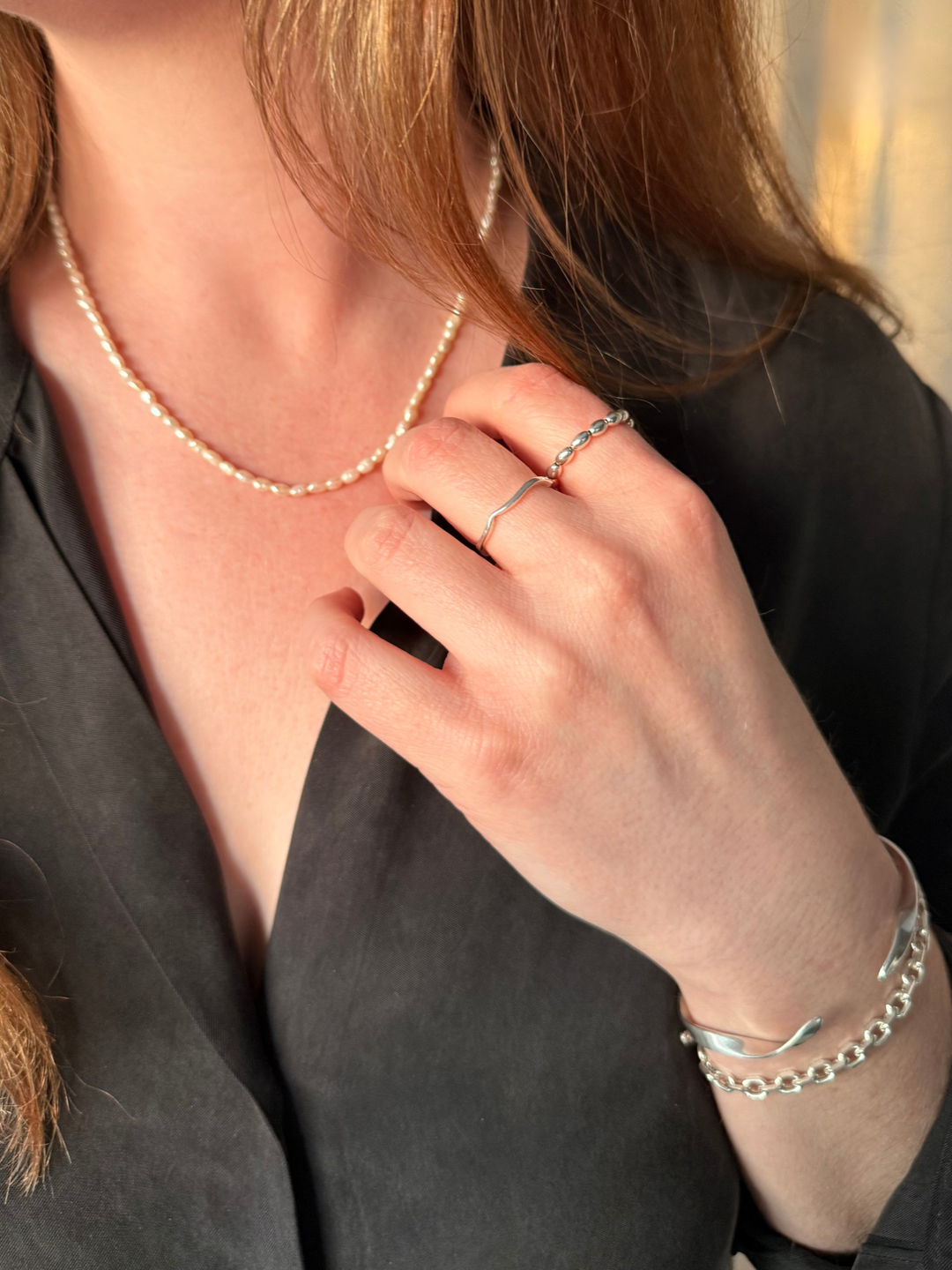 Woman wearing Nusands pearl choker necklace, silver rings, and bracelets with a blurred background