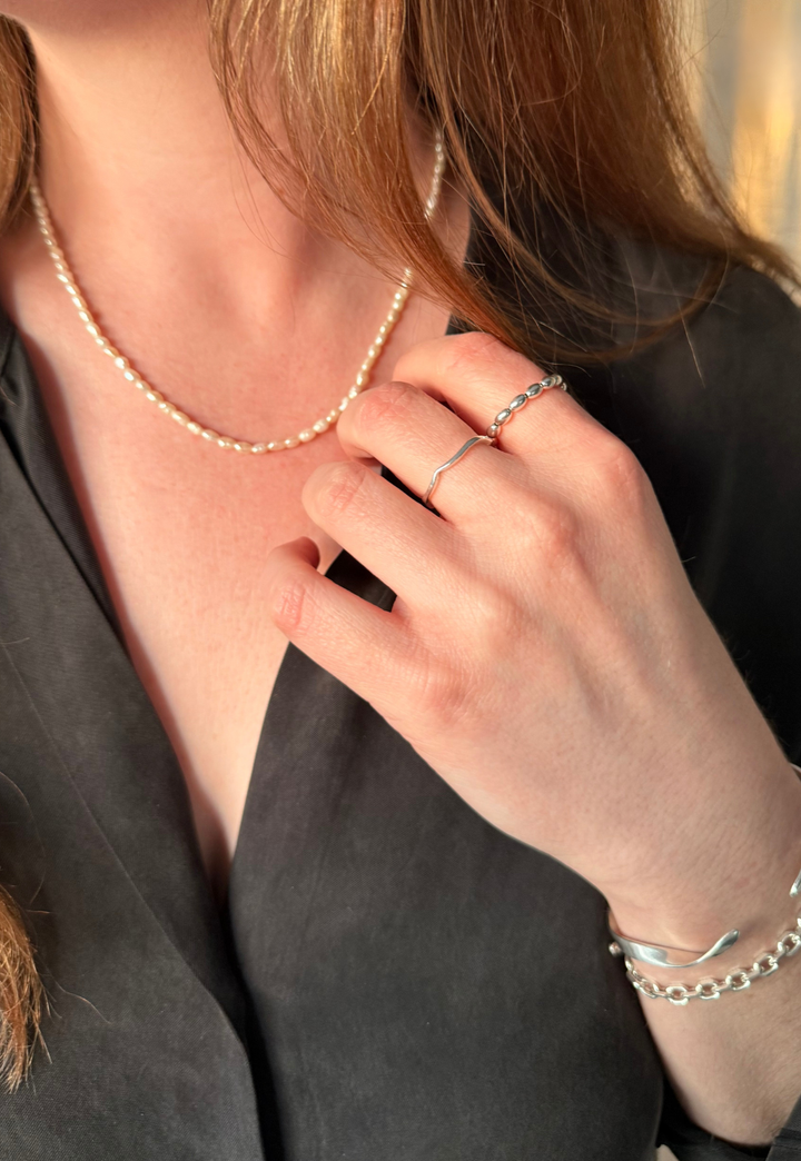 Woman wearing Nusands pearl choker necklace, silver rings, and bracelets with a blurred background