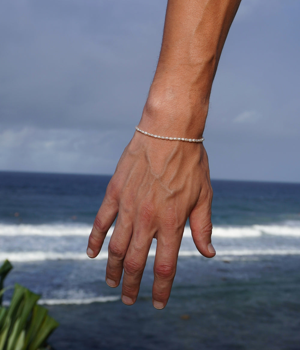 Corey wearing Unisex Pearl Bracelet on his right arm holding it down in front of the beach and ocean waves to show the freshwater pearls on his right wrist.