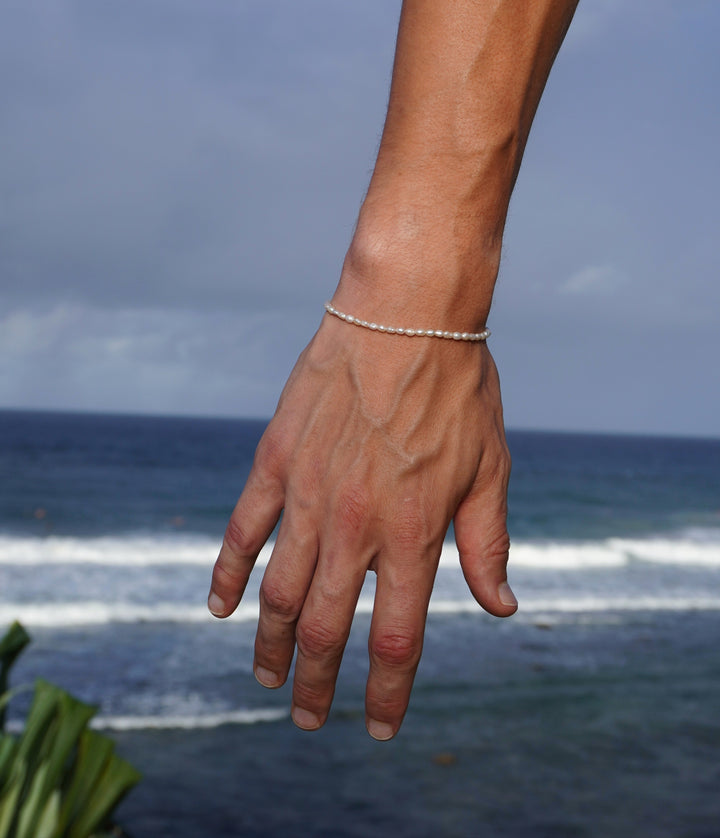 Corey wearing Unisex Pearl Bracelet on his right arm holding it down in front of the beach and ocean waves to show the freshwater pearls on his right wrist.