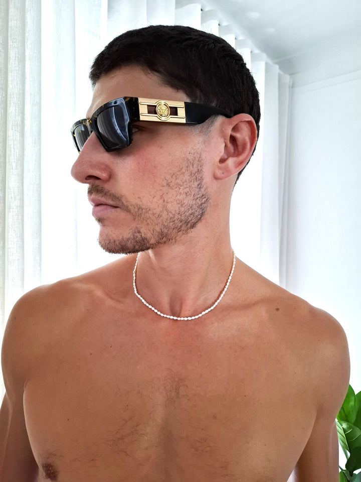Corey Chest up shot, looking away from camera wearing dainty sterling silver fresh water Pearl Necklace around his neck and Versace sunglassed.