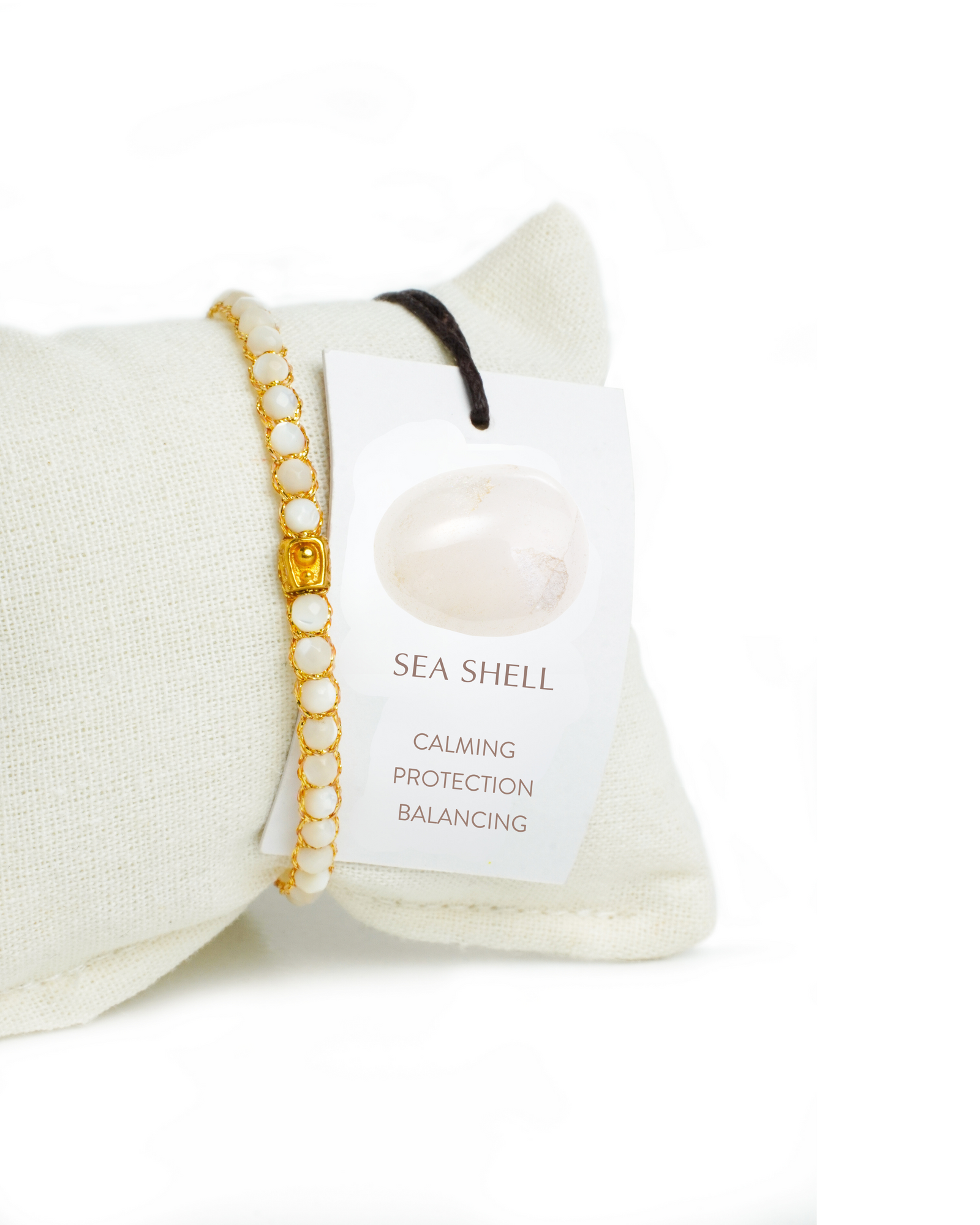 Sea Shell Gemstone Adjustable bracelet covering white cushion strung together with 18K Gold Yarn, Information tag showing.