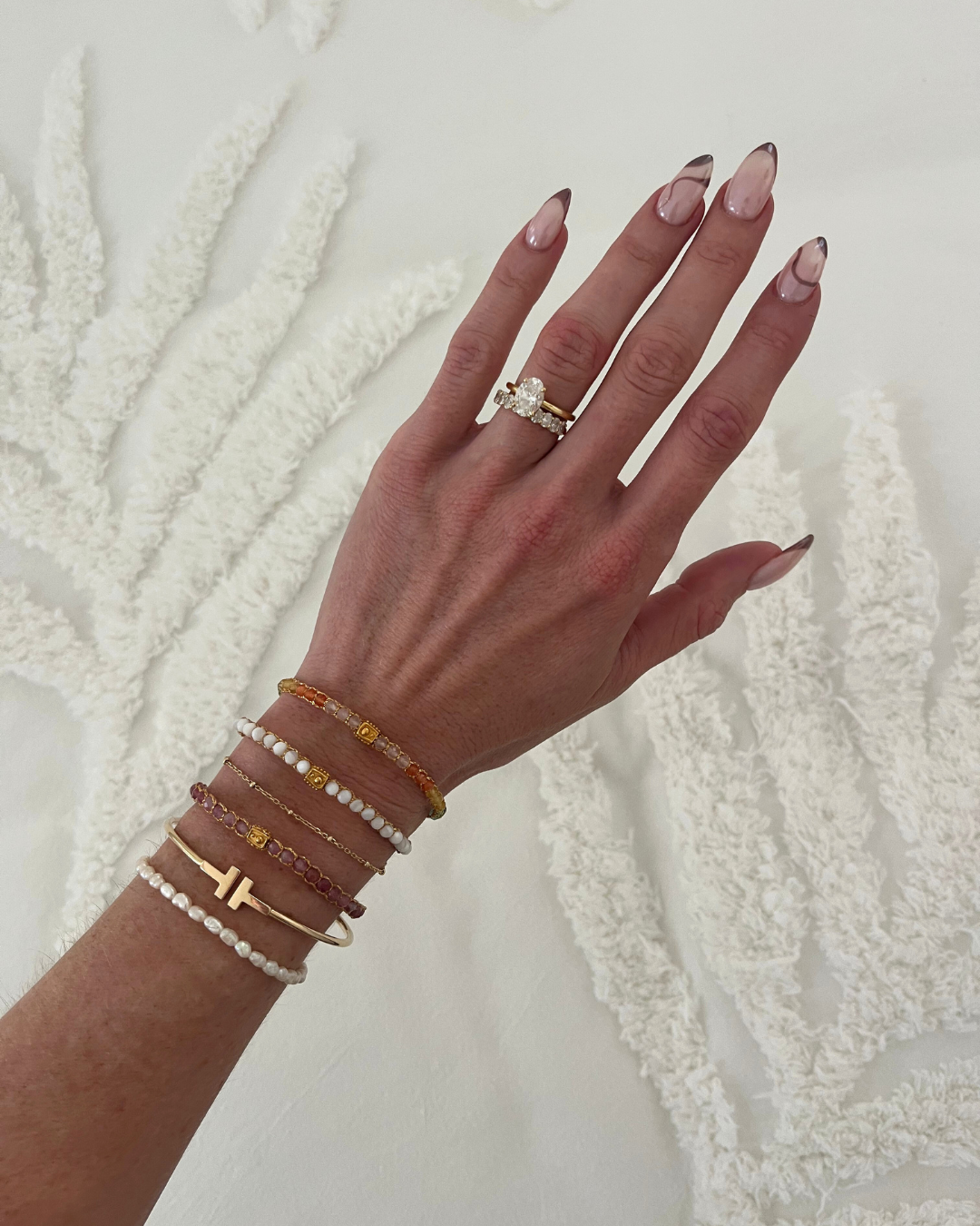 Hand wearing multiple gemstone bracelets on a textured white background