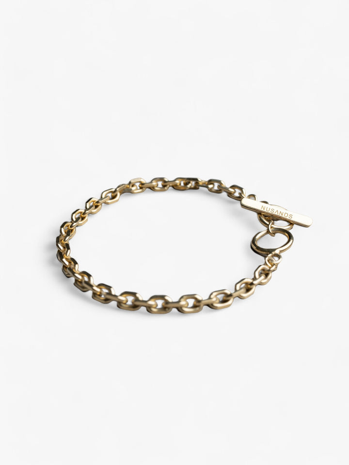 Thick 18k gold chain link bracelet with nusands logo clasp laying in a circle