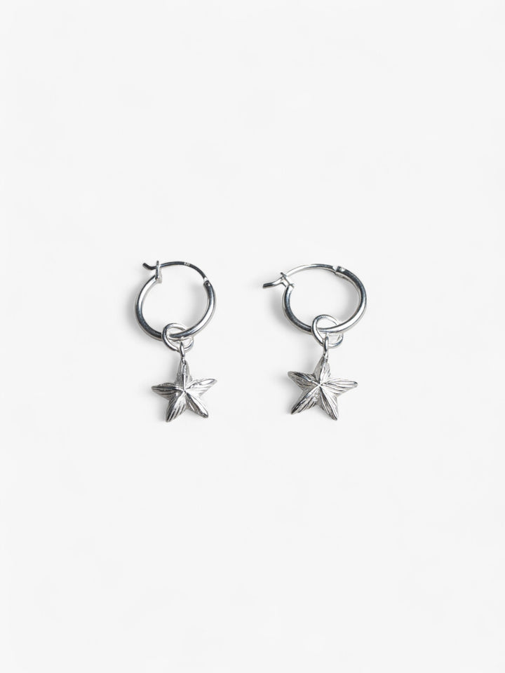 Pair of sterling silver round hoop earrings with removable star charms laying flat next to each other.