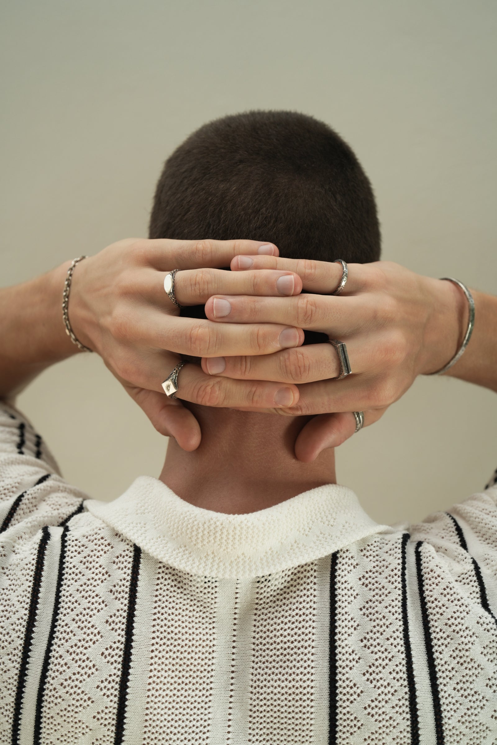 Founder of Nusands Corey Micari with hands clasped behind head wearing sterling silver shackled bracelet, suns out and mirrored signet ring on left hand, striking cuff, stacker, line in the sand and blade ring on right hand.