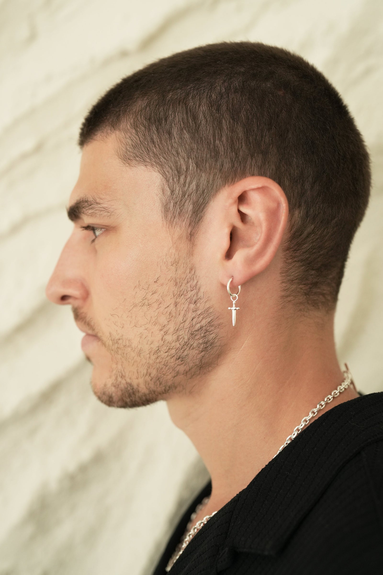 Founder of Nusands Corey Micari side profile wearing sterling silver hoop earrings with removable sword charm in left ear